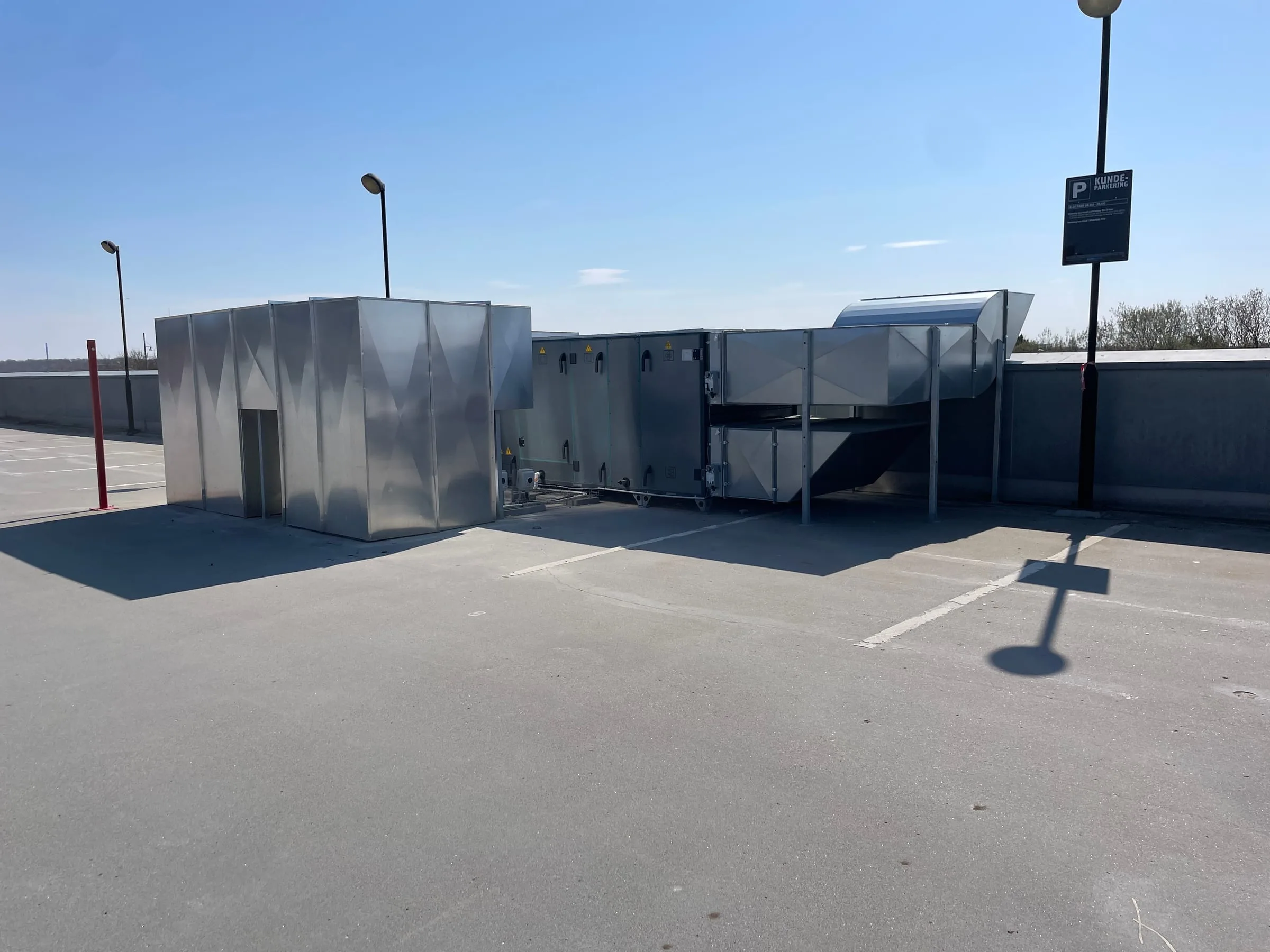 Aggregater, kanaler og en inddækning af blanke metalplader udendørs på et parkeringsdæk, AB Clausen HQ, Glostrup
