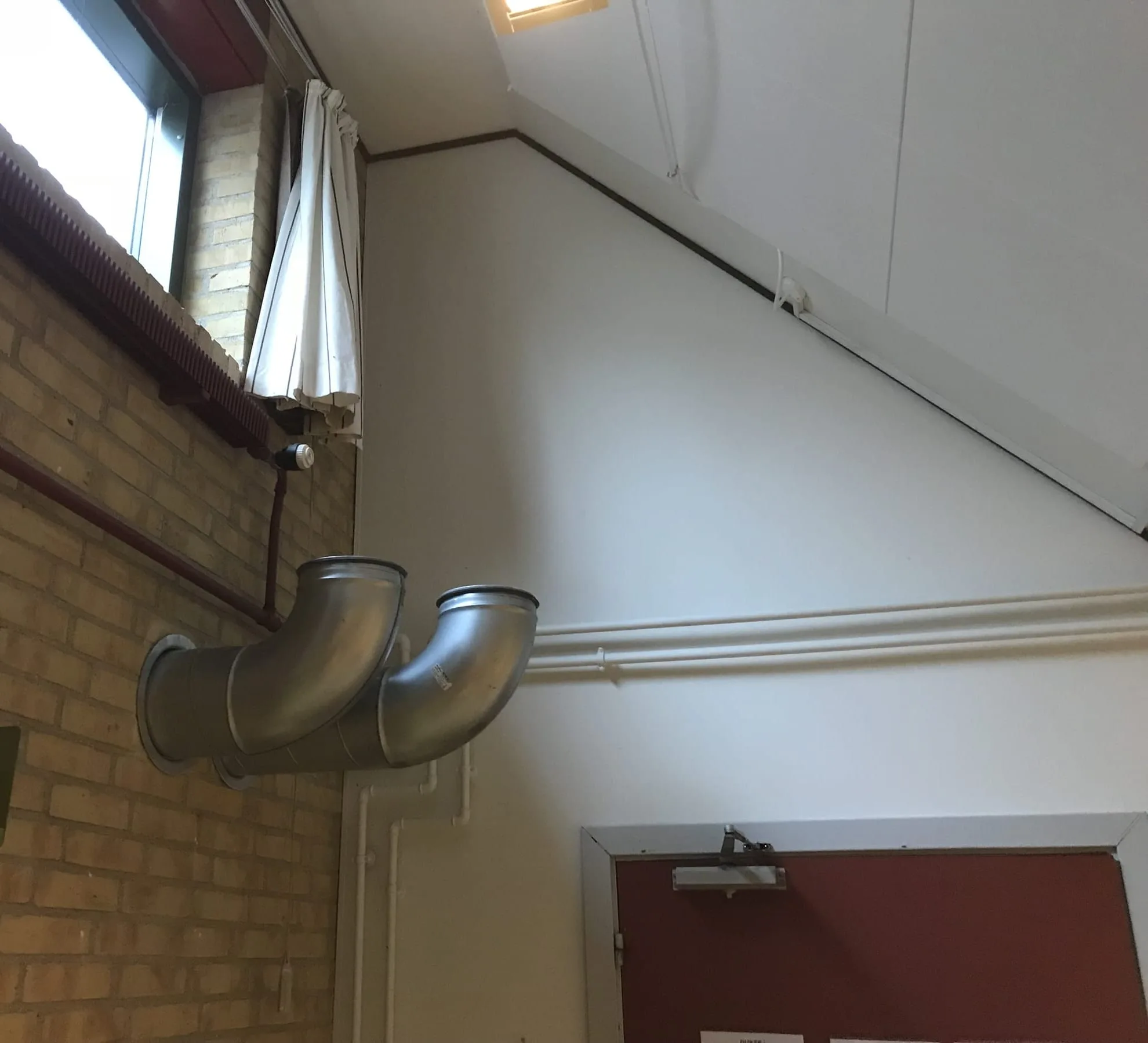 To kanalbøjninger fra murstensvæggen under det skrå loft i et klasselokale, Ravnsholtskolen, Allerød